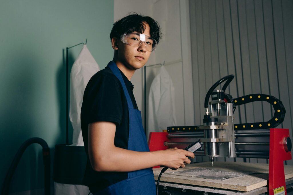 Asian engineer working with a CNC machine while wearing safety glasses. Industrial setting indoors.