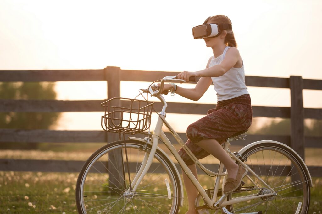 A teenager enjoys virtual reality while riding a bicycle outdoors at sunset.