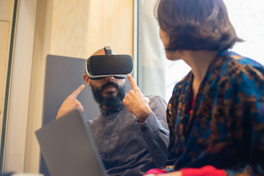 A man and woman explore virtual reality technology indoors with a laptop and VR goggles.